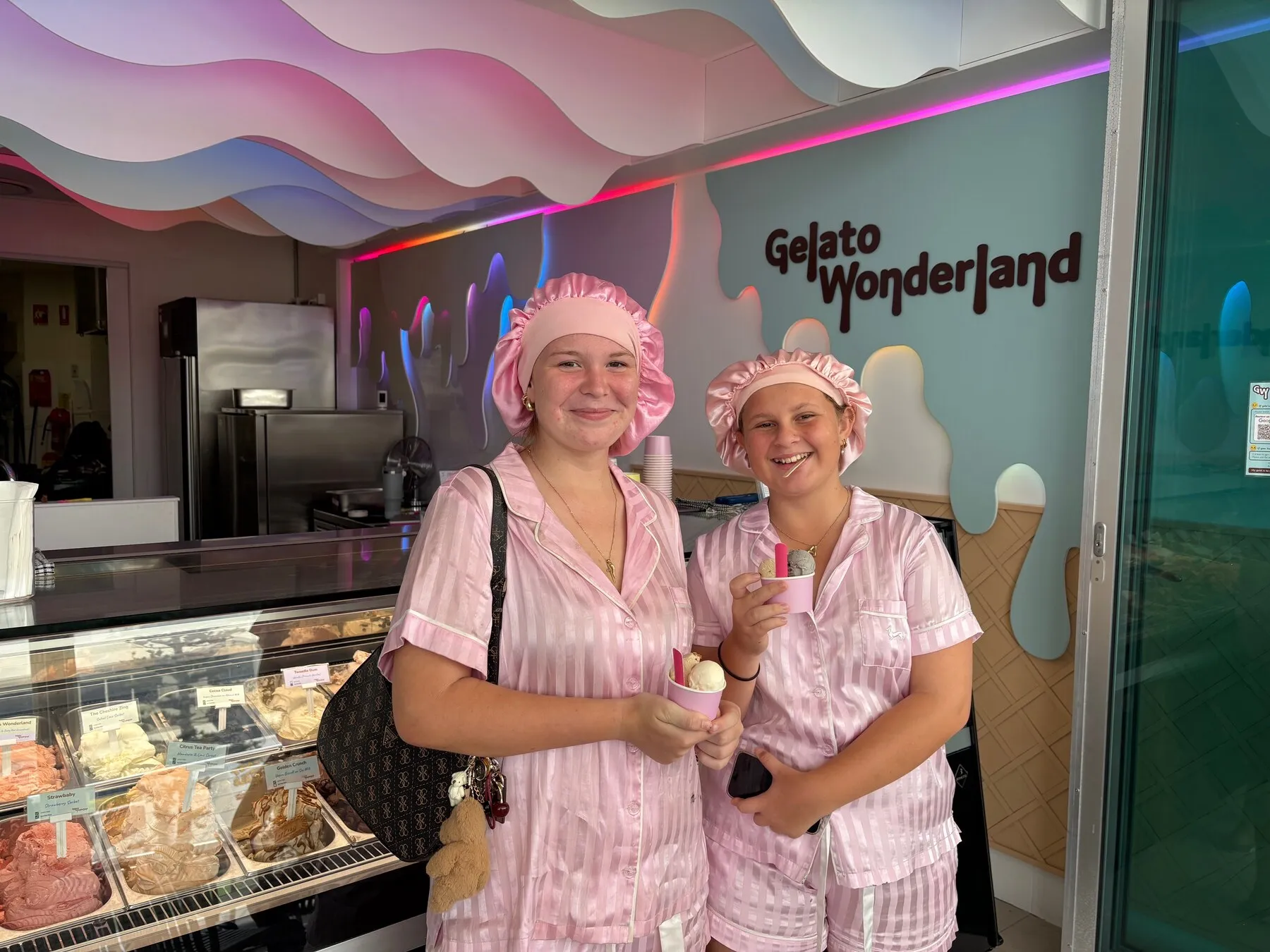 Two smiling visitors holding cups of gelato beside the cabinet.